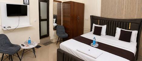 A hotel room with a bed, a desk, a chair, an air conditioning unit, a television, and a wardrobe.