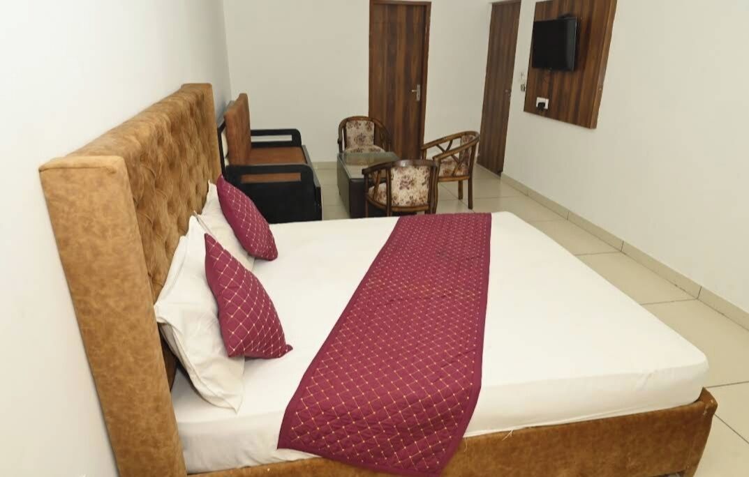 A bedroom with a bed, pillows, a blanket, a wooden headboard, a small table with chairs, and a TV mounted on the wall.