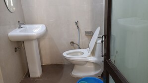 A small bathroom with a white sink, toilet, and blue bucket. - Hotel sudan inn kalka shimla higway  (Zirakpur)