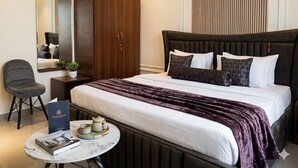 A hotel room with a bed, a desk with a chair, a small table with a book and teapot, a wardrobe, and a mirror. - Hotel sudan inn kalka shimla higway  (Zirakpur)
