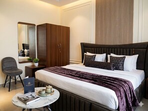 Habitación de hotel con cama, escritorio con silla, mesita con un libro y tetera, armario y espejo.
