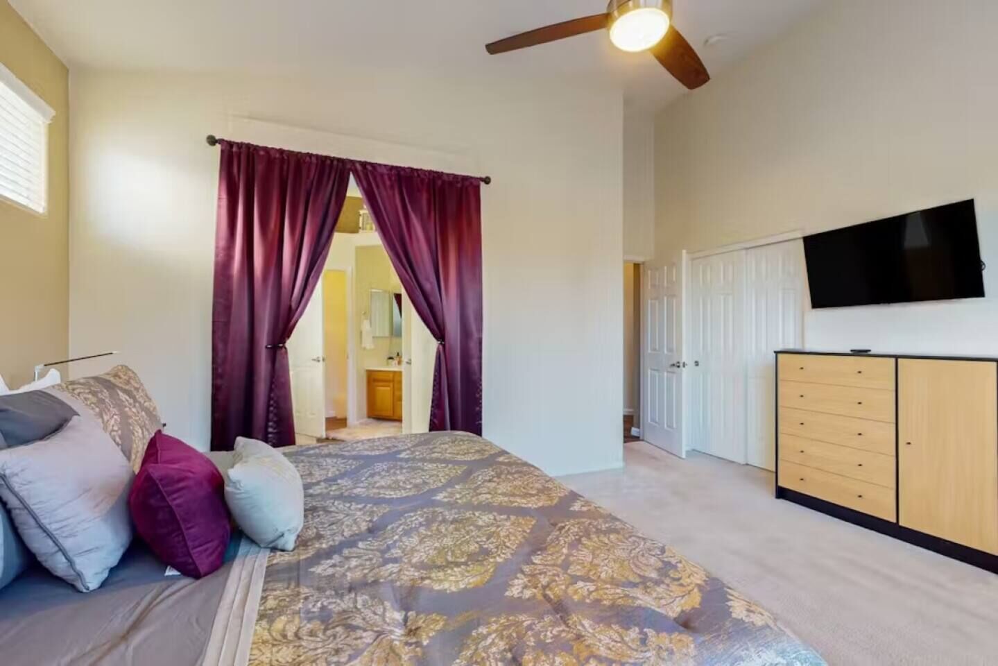 Ein Schlafzimmer mit Bett, Vorhängen, Deckenventilator, Fernseher und Kleiderschrank.