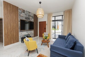 A modern living room with a sofa, yellow chairs, a TV, and a stone wall. - 3-bedroom house in peaceful Punta Cana with cool AC (Punta Cana)