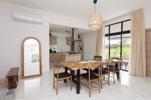 A dining area with a wooden table and chairs, a hanging light fixture, and a view of the kitchen and outside. - 3-bedroom house in peaceful Punta Cana with cool AC (Punta Cana)