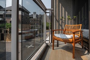 Ein Balkon mit einem Holzstuhl, einer Glastür und Blick auf Gebäude.