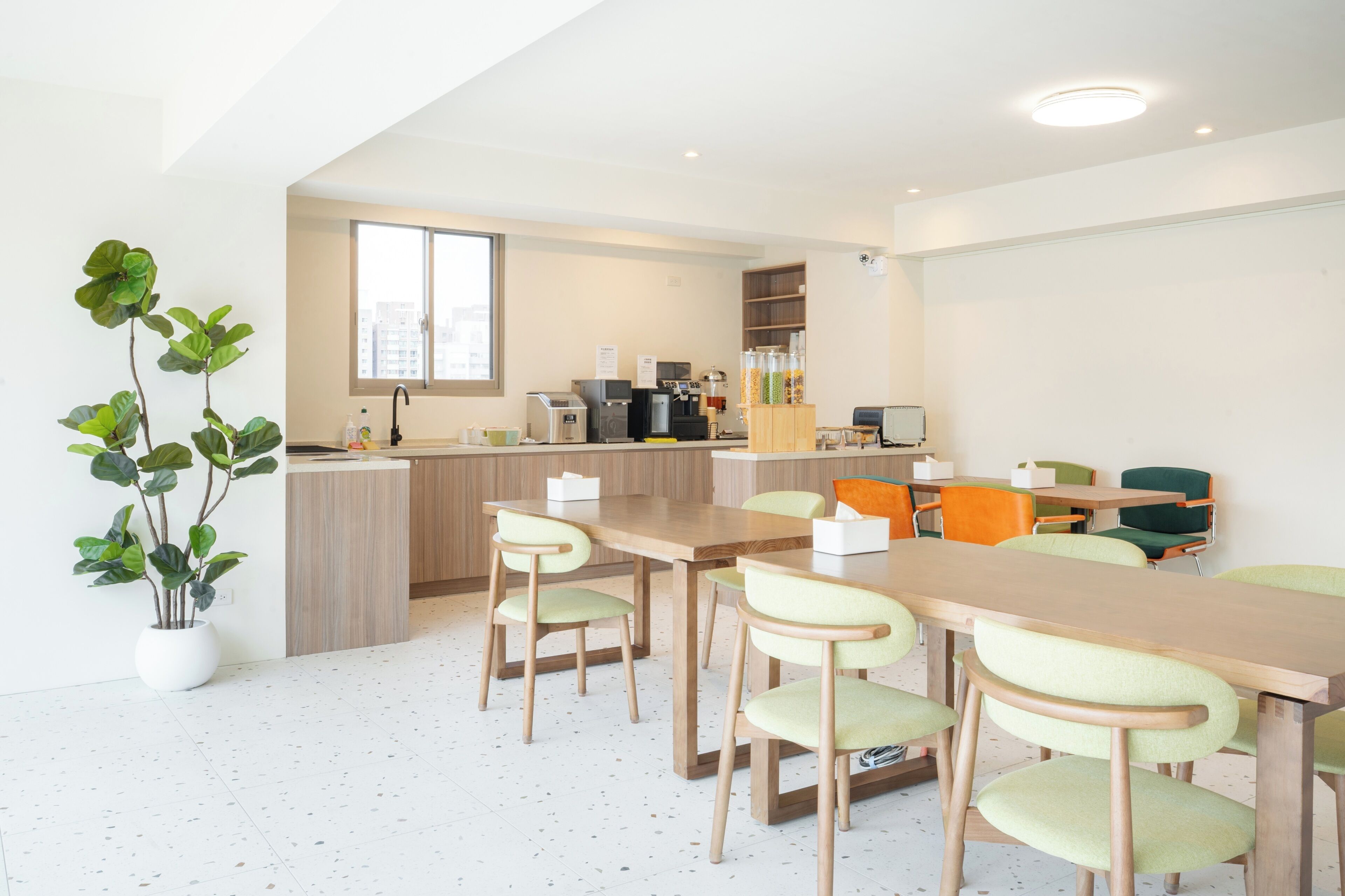 A modern kitchen with a dining area, including a long wooden table and chairs, a potted plant, and a view of the city.