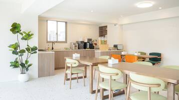 A modern kitchen with a dining area, including a long wooden table and chairs, a potted plant, and a view of the city.