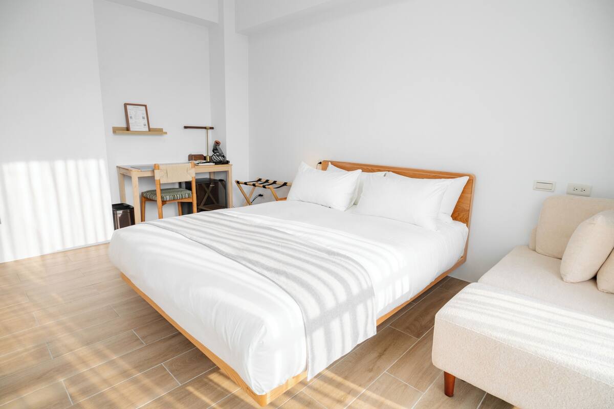 A bedroom with a wooden bed, a small desk, a chair, and a sofa.