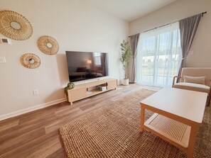 Uma sala de estar moderna com televisão de tela plana, um sofá, uma mesa de jantar e uma janela grande com cortinas.