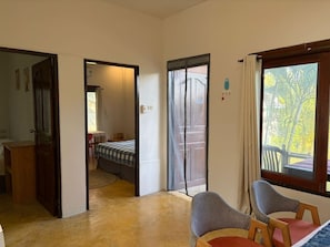 Ein Zimmer mit einem Bett, einem Sessel, einem Schreibtisch und einem Fenster mit Blick auf Bäume.