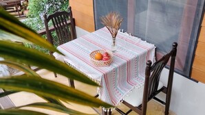 Een tafel met een tafelkleed met patroon, een vaas met gedroogde planten en een mand vol fruit.