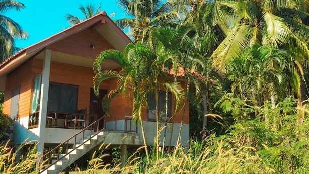 Een bungalow met balkon, omringd door palmbomen en begroeiing.