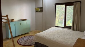 Een slaapkamer met een bed, een kledingkast, een raam met gordijnen en een airconditioning.
