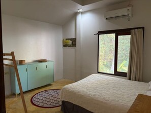 Ein Schlafzimmer mit einem Bett, einem Kleiderschrank, einem Fenster mit Vorhängen und einer Klimaanlage.