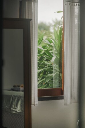 Una stanza con finestra, tende, un letto e un comodino.