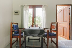 A room with a table set for two, two chairs, a window with curtains, a door, and a thermostat on the wall. - Entire Private House 2BR - Heart of Thong Sala (Tambon Ko Pha-ngan)