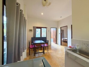 A compact room with a dining table, chairs, a kitchen area with a sink, and a view of the outside through a window. - Sunset View - Home near Beach (300m.) - 2 BR (ตำบลเกาะพะงัน)