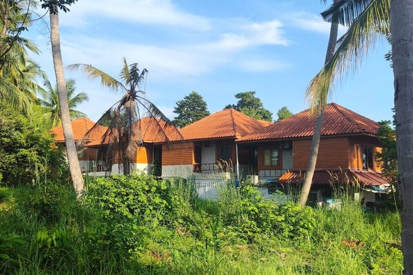 A bungalow-style building with a tiled roof, surrounded by lush greenery and palm trees. - Sunset View - Home near Beach (300m.) - 2 BR (ตำบลเกาะพะงัน)