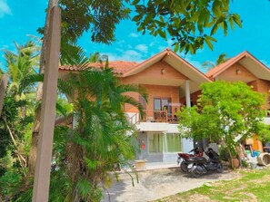 A bungalow with a balcony, surrounded by lush greenery and palm trees. - Sunset View - Home near Beach (300m.) - 2 BR (ตำบลเกาะพะงัน)
