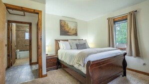 Quarto com cama de madeira, um quadro na parede, janela com cortinas e porta para outro cômodo.