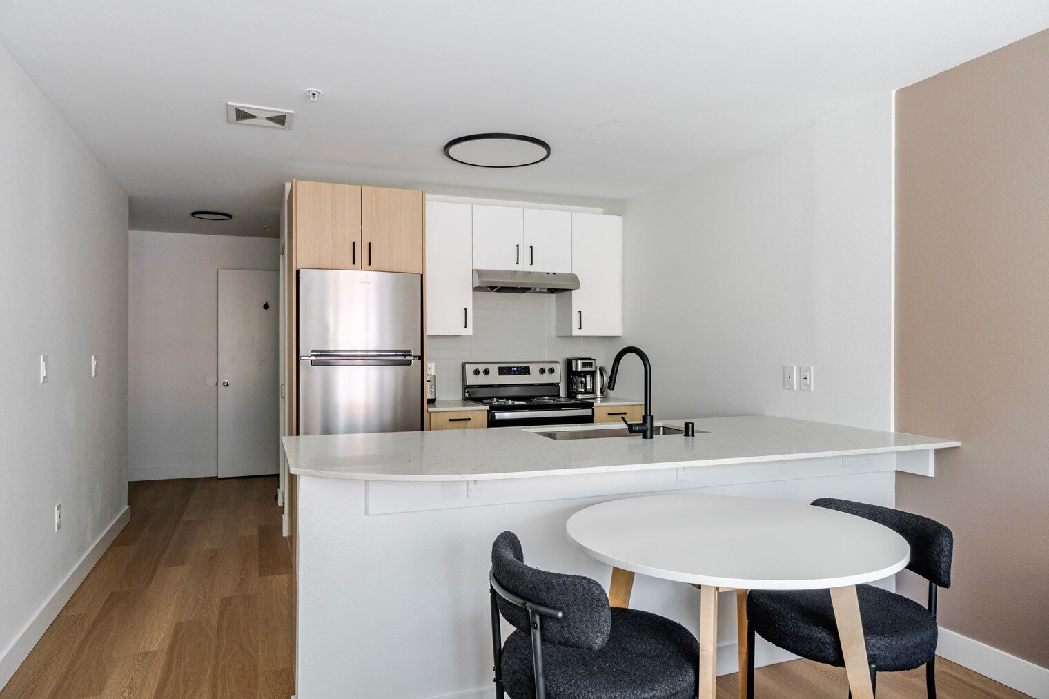 A compact kitchen with a built-in refrigerator, stove, and sink, a small dining area with two chairs, and a white countertop.
