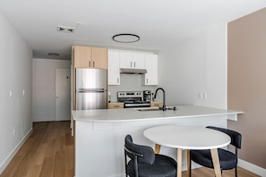 A compact kitchen with a built-in refrigerator, stove, and sink, a small dining area with two chairs, and a white countertop. - Blueground | Denny Triangle, fitness center, nr Seattle Art Museum (Seattle)