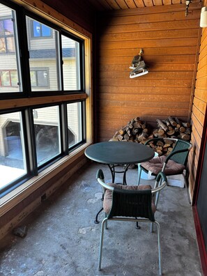 Ein Eckzimmer mit großem Fenster, einem runden Tisch, zwei Stühlen und einem Holzstoß.
