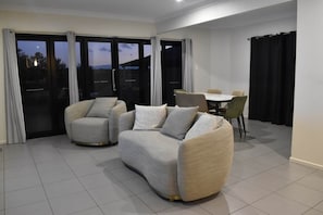 A modern living room with a sofa set, a dining table with chairs, and a sliding glass door leading to an outdoor area. - The Duncan Retreat Bald Hills QLD (Bald Hills)