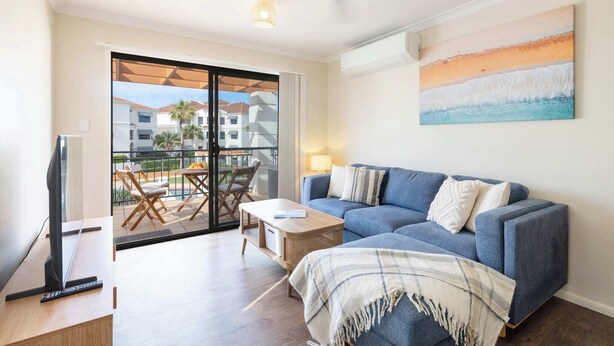 Una sala de estar moderna con un sofá azul, un televisor y un balcón con mobiliario exterior.