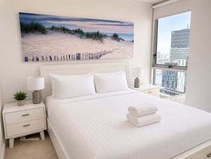 A hotel room with a large bed, a nightstand, a lamp, a small plant, and a city view. - Brisbane CBD Skyline Stay + Resort Amenities (Brisbane)