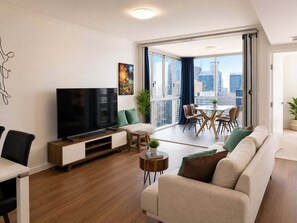 A modern living room with a flat-screen TV, a sofa, a dining table with chairs, and a balcony with a city view. - Brisbane CBD Skyline Stay + Resort Amenities (Brisbane)