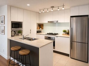 A modern kitchen with white cabinetry, a stainless steel refrigerator, a built-in microwave, and a gas stove. - Brisbane CBD Skyline Stay + Resort Amenities (Brisbane)