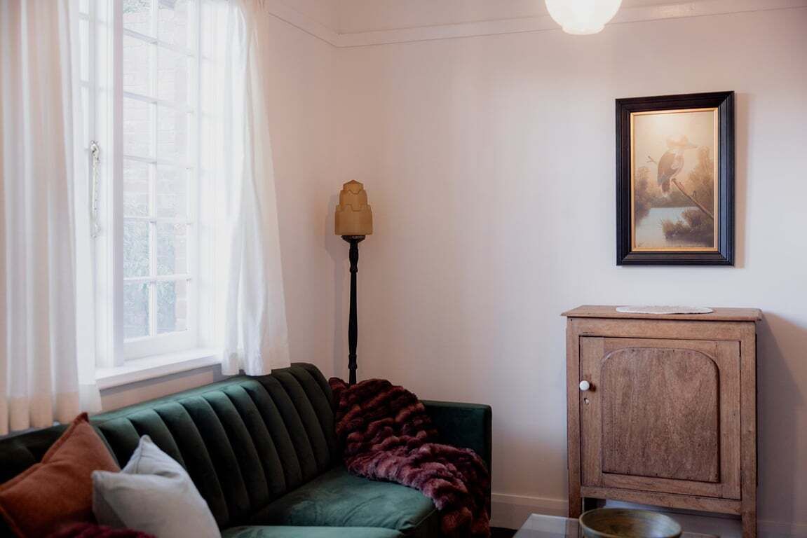 Ett rum med en grön soffa, ett träskåp, en inramad tavla på väggen och en golvlampa.