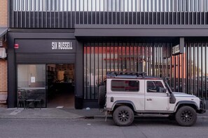 Un SUV blanco estacionado frente a un edificio de fachada negra con el nombre 'SIX RUSSELL' a la vista en la entrada.