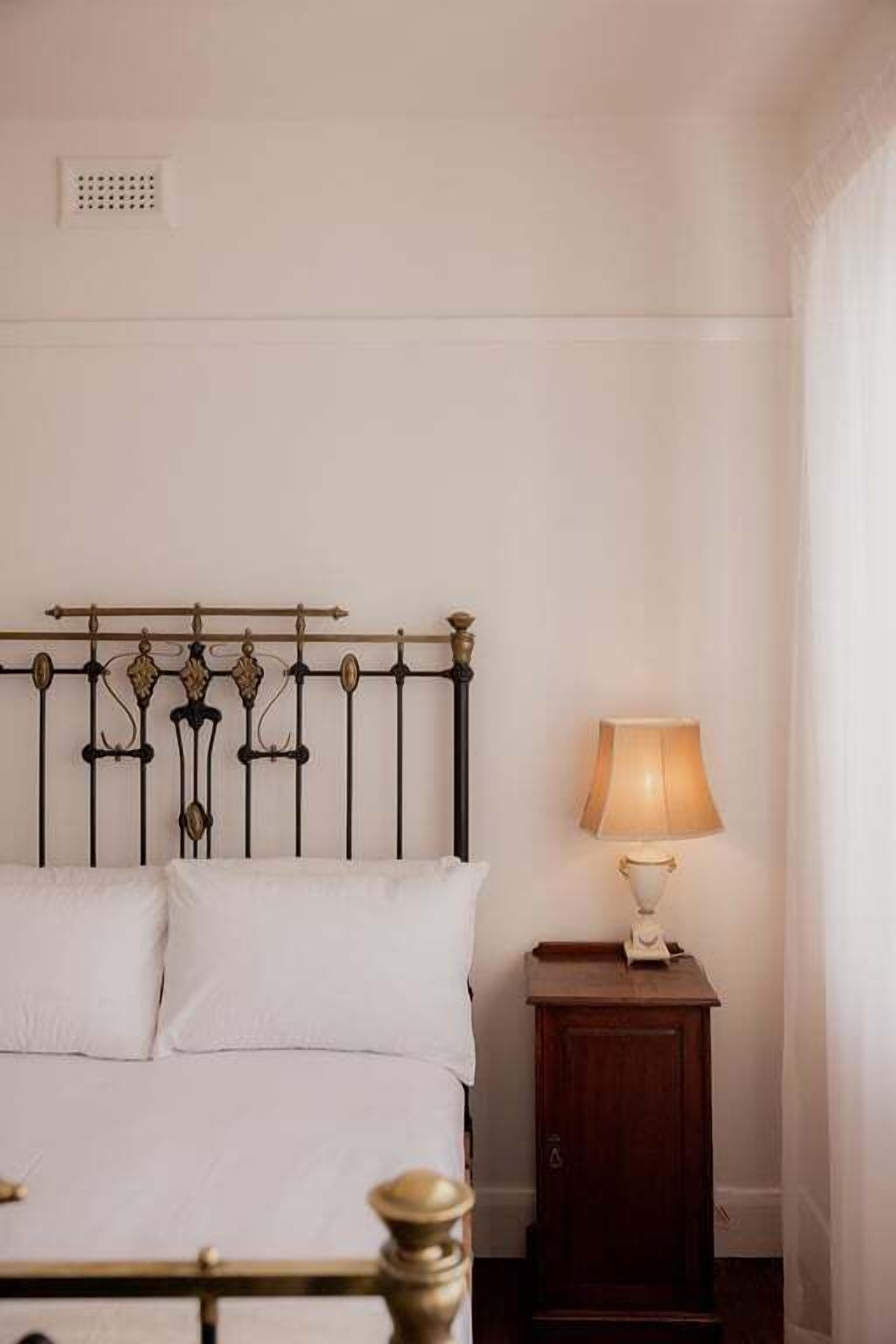 A bed with a metal headboard, a bedside table with a lamp, and a wall-mounted light fixture.