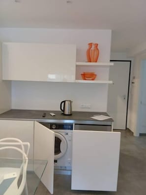 Una cocina compacta con lavadora, cafetera y una mesa de vidrio.