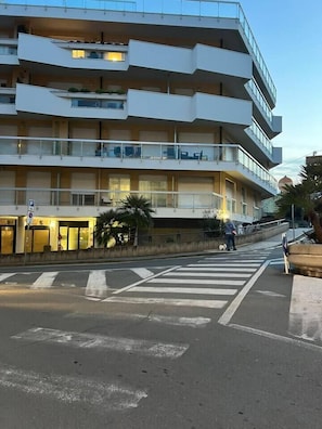 Un edificio de varios pisos con balcones, un paso de peatones y una calle.
