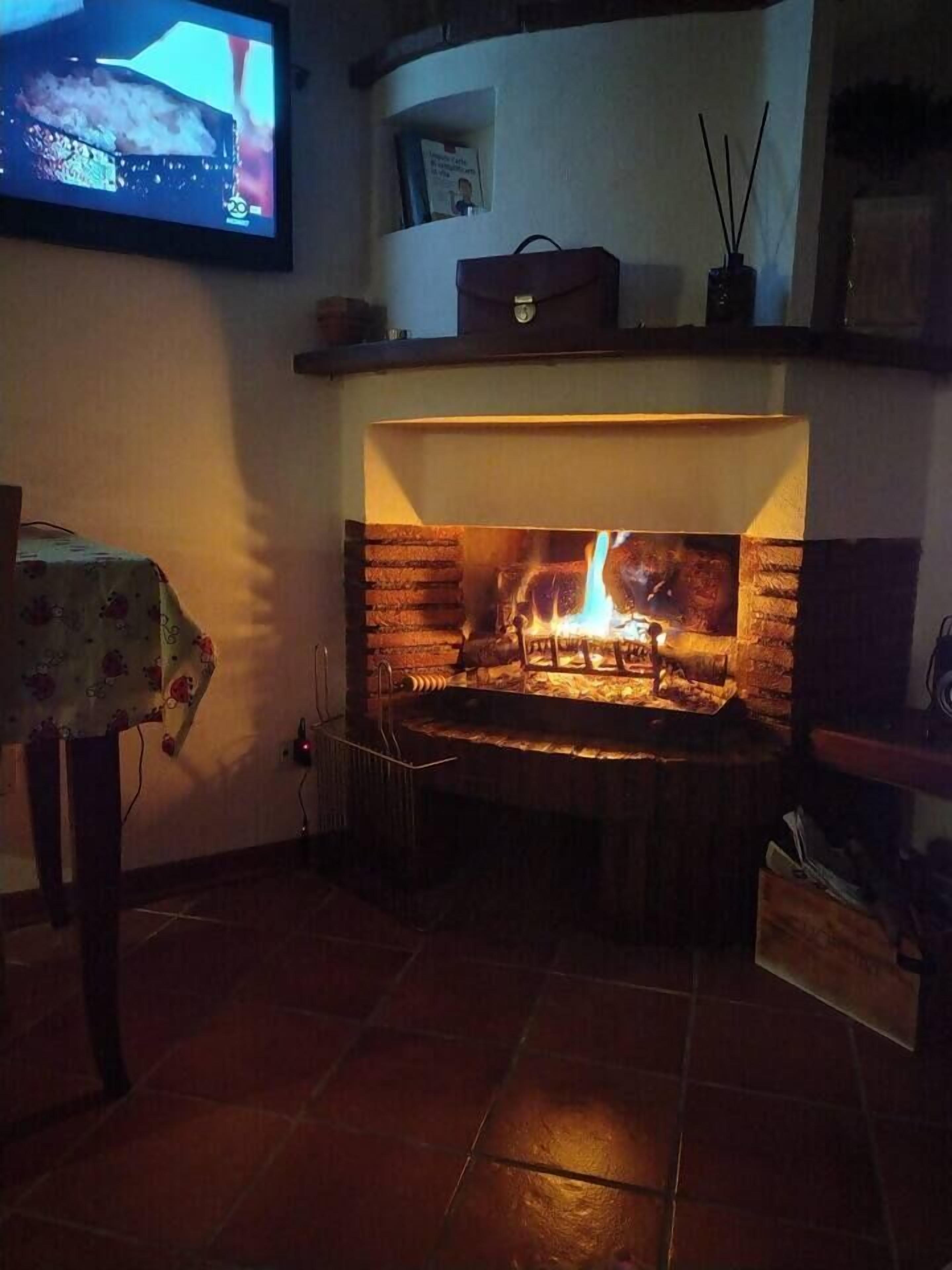 Una chimenea con un televisor montado encima, una mesa con mantel floral y una pared de ladrillo.