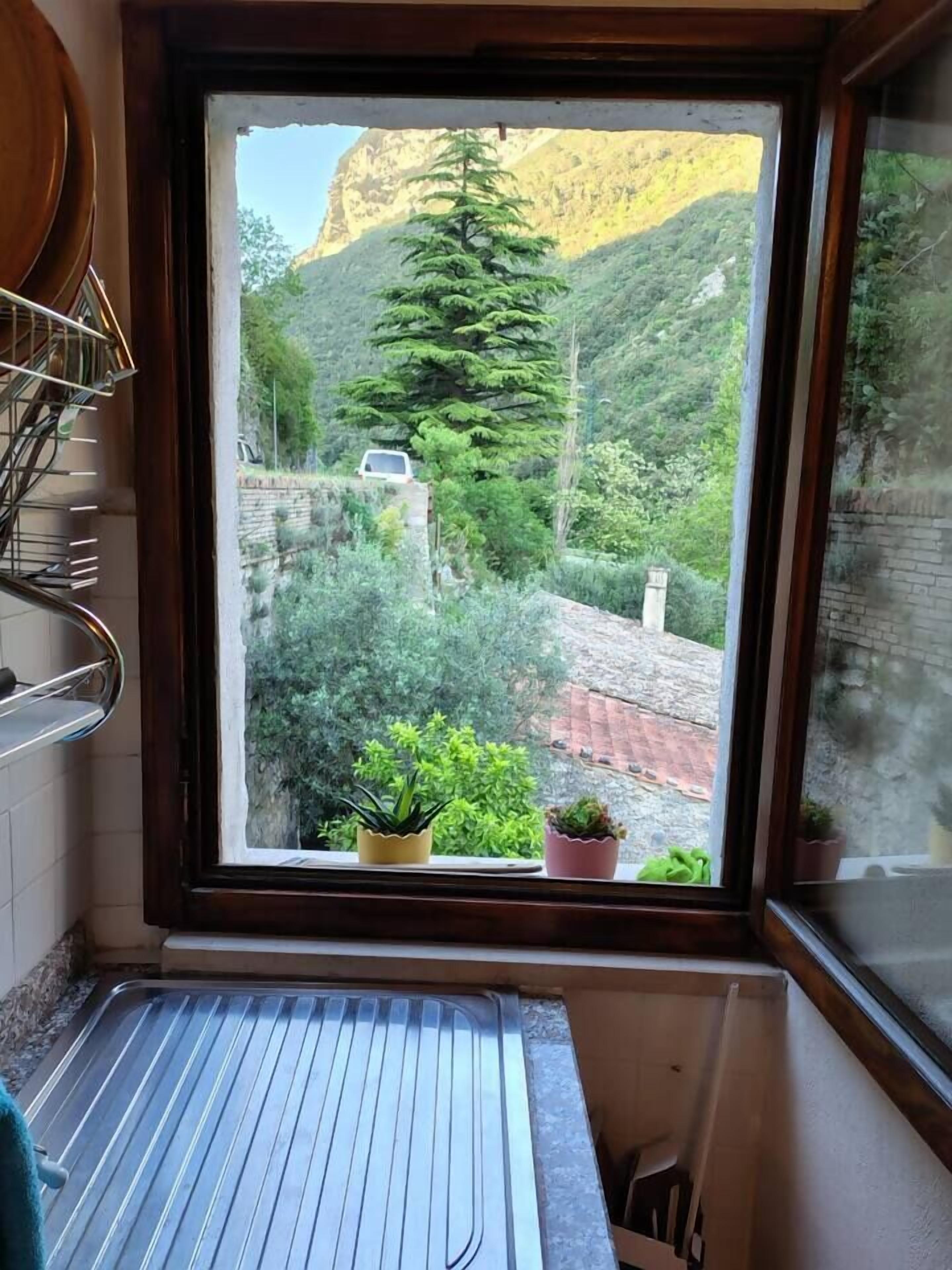 Una finestra con vista su un paesaggio montuoso, una stendibiancheria in metallo e piante in vaso sul davanzale.