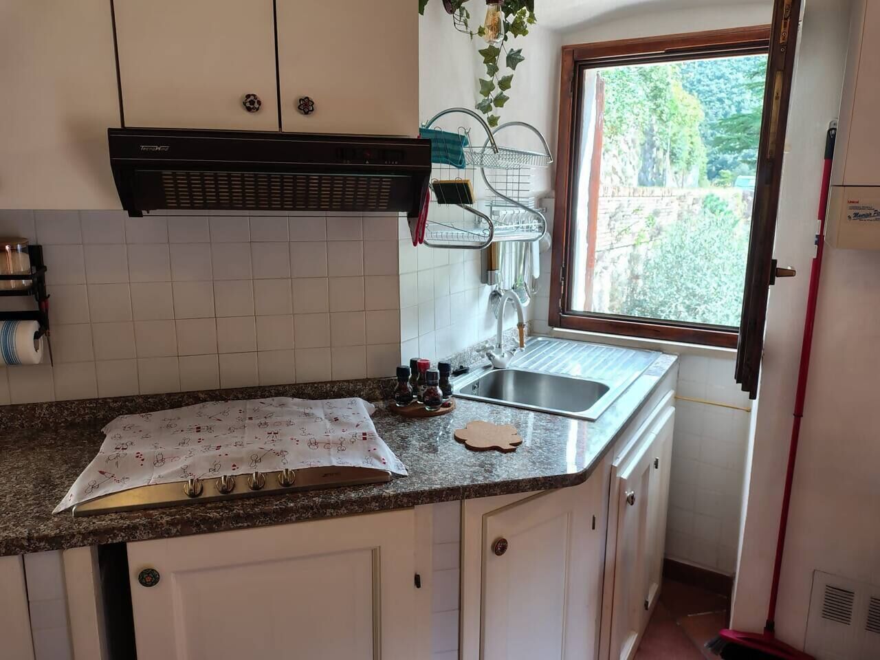 A kitchen with white cabinets, a granite countertop, a window, and a built-in range hood.