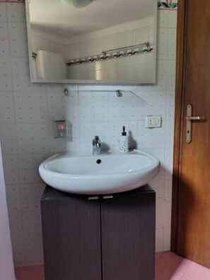 Une salle de bain avec un lavabo blanc, un miroir au-dessus et une porte en bois.