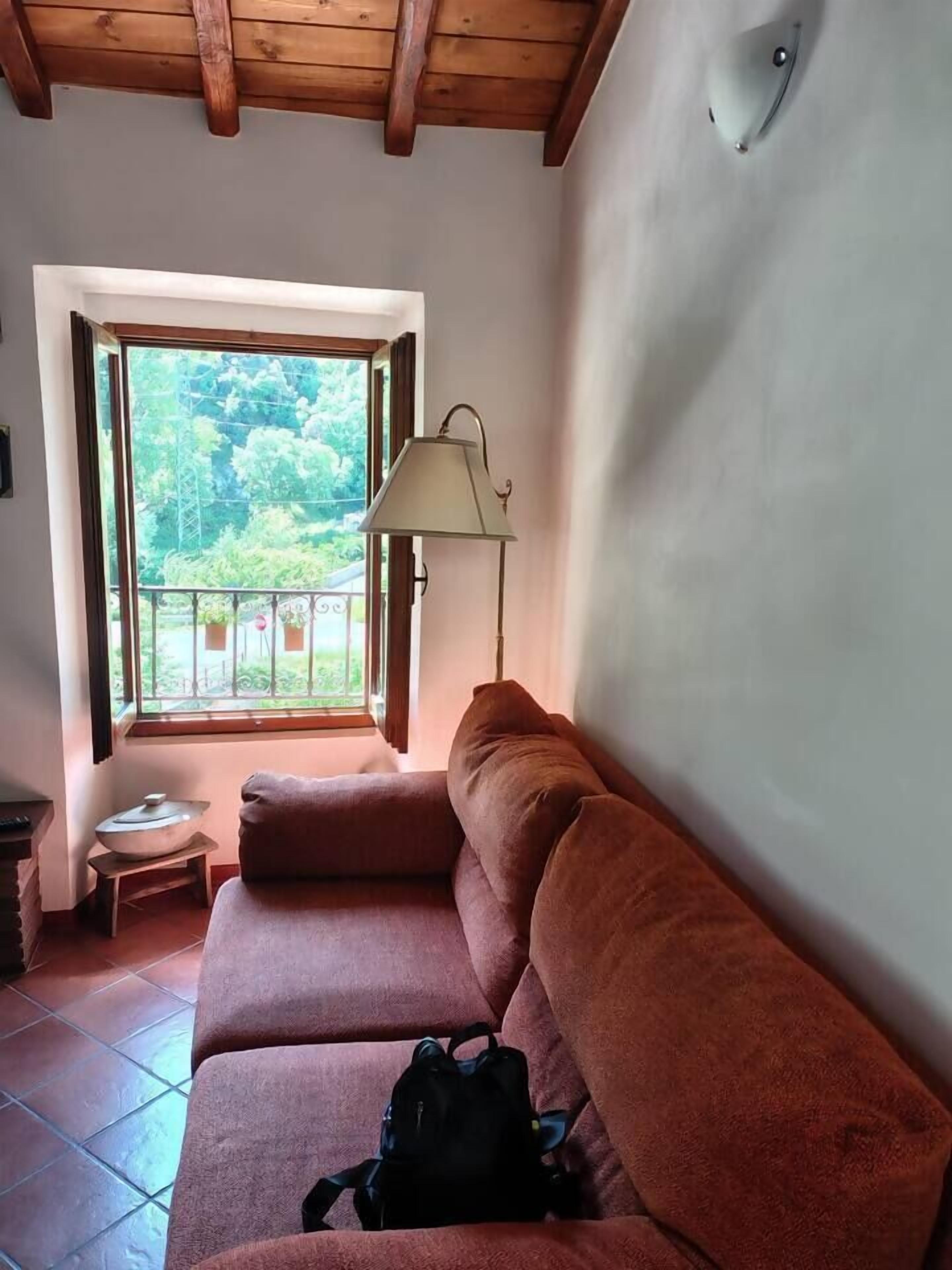 Une pièce comprenant un canapé, une lampe, une petite table et une fenêtre donnant sur un paysage verdoyant.