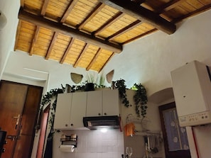 Una cocina con salpicadero de azulejos, vigas de techo de madera y un mueble blanco con campana extractora integrada.