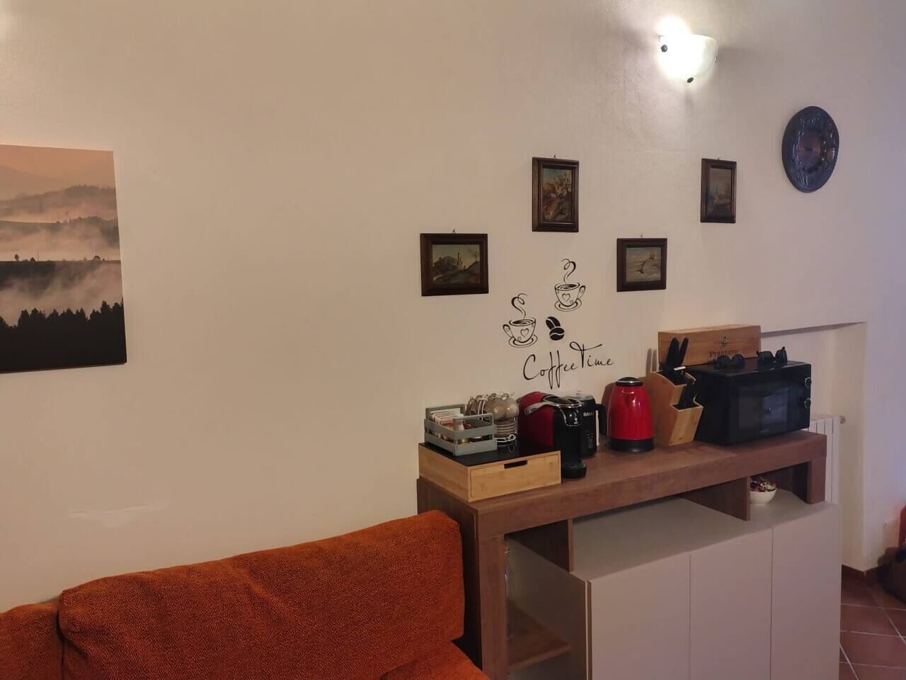 A cozy living area with a wooden coffee table, a red kettle, a coffee machine, and a framed picture on the wall.