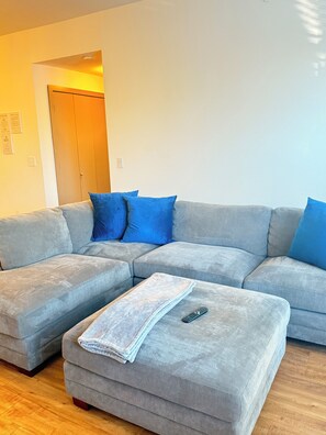 A living room with a grey sectional sofa, a matching ottoman, and blue cushions. - Cozy 1-bedroom apartment near addison square (Dallas)