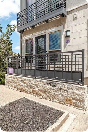 A building with a stone facade, a metal balcony, and a gated entrance. - Cozy 1-bedroom apartment near addison square (Dallas)