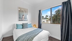 A bedroom with a large bed, a window with curtains, a wall-mounted artwork, and a bedside lamp. - Lakeside 2-bed Retreat With Sunny Balcony (Buff Point)