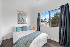 Um quarto com uma cama grande, uma janela com cortinas, uma obra de arte na parede e um abajur.