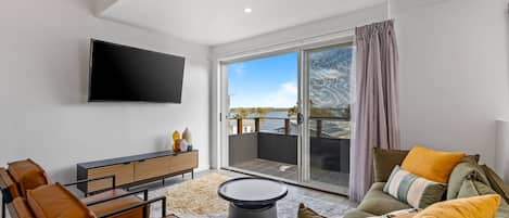 En moderne stue med et fladskærms-tv, læder møbler, et rundt sofabord og en skydedør af glas, der fører ud til en balkon.