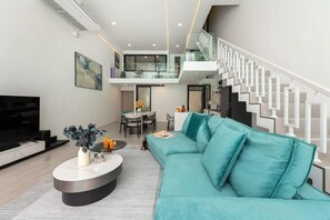 A modern living room with a teal sofa, a flat-screen TV, and a dining area with a glass railing. - Comfy Townhouse Near Fisherman (Bophut)